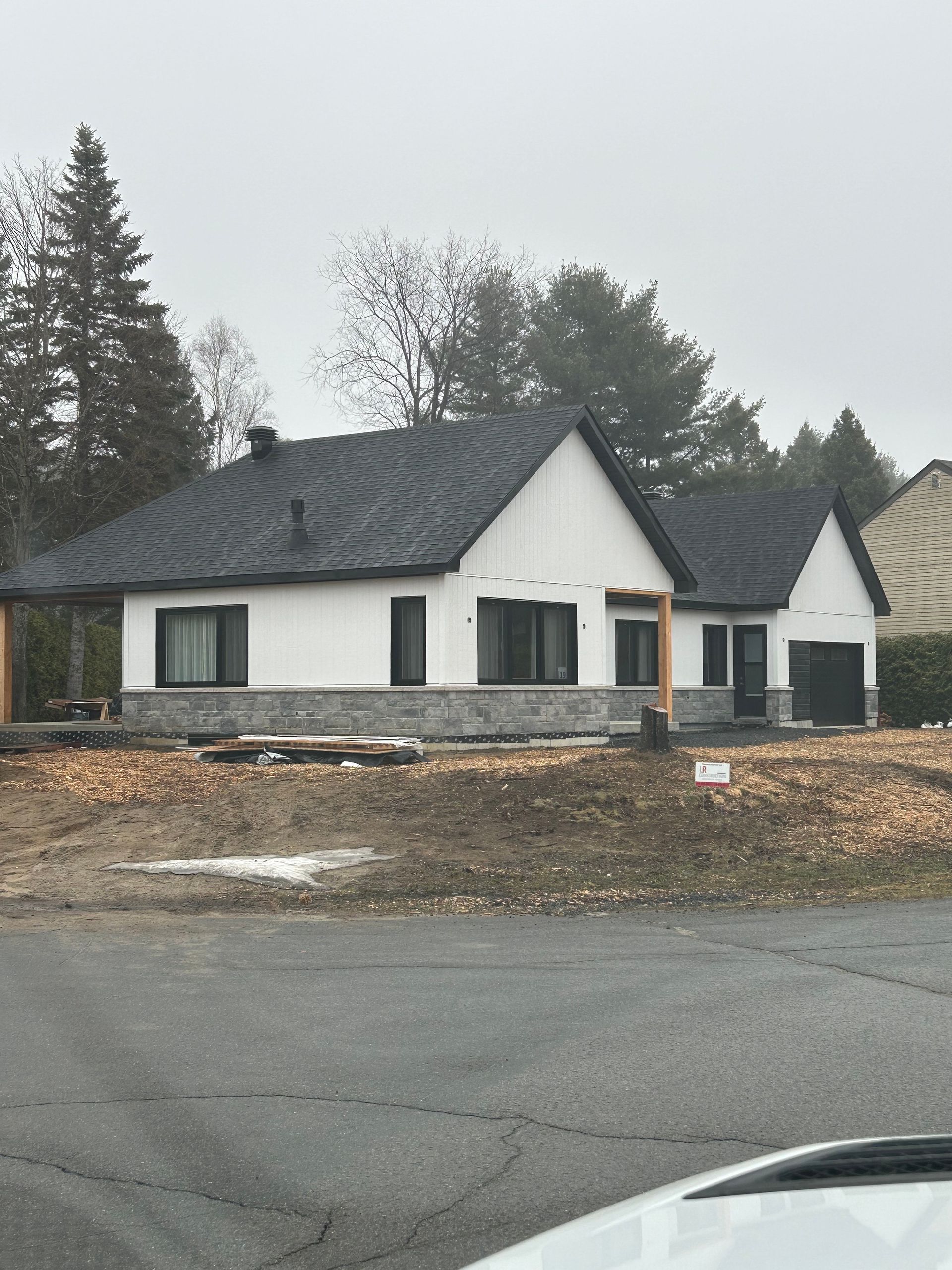 Une maison blanche au toit sombre et à la façade en pierre, par une journée grise et nuageuse.
