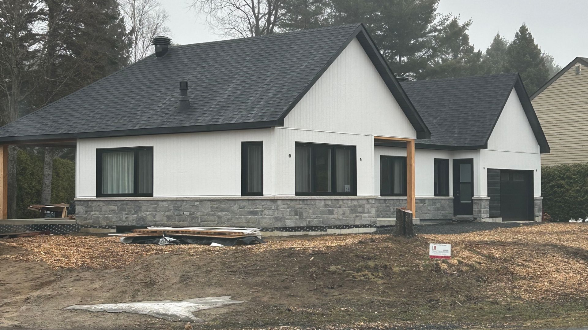 Maison blanche moderne avec soubassement en pierre grise, toit et fenêtres noirs, située dans une cour.
