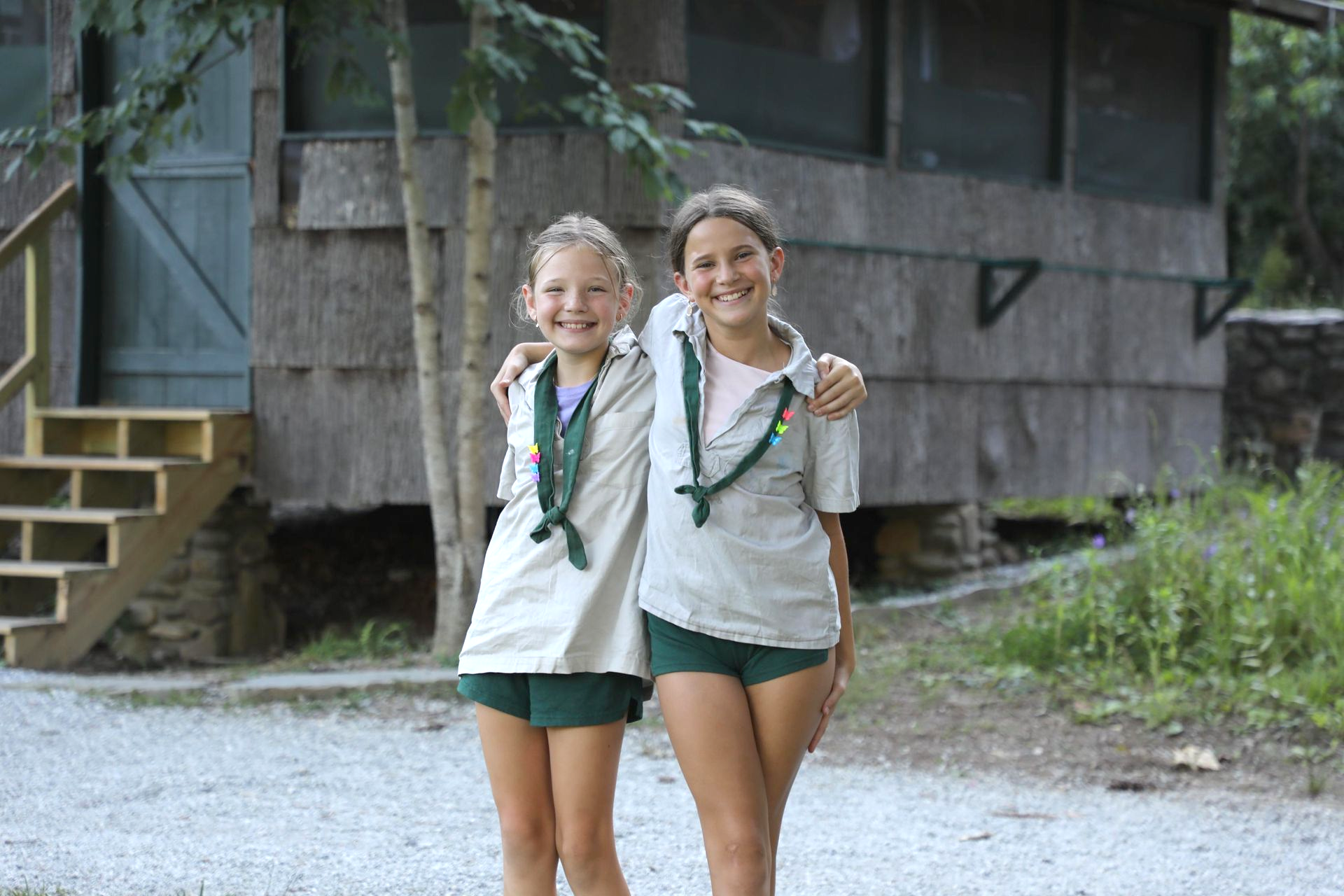 Two scouts with arms around each other smiling in front of a rustic wooden building with steps.