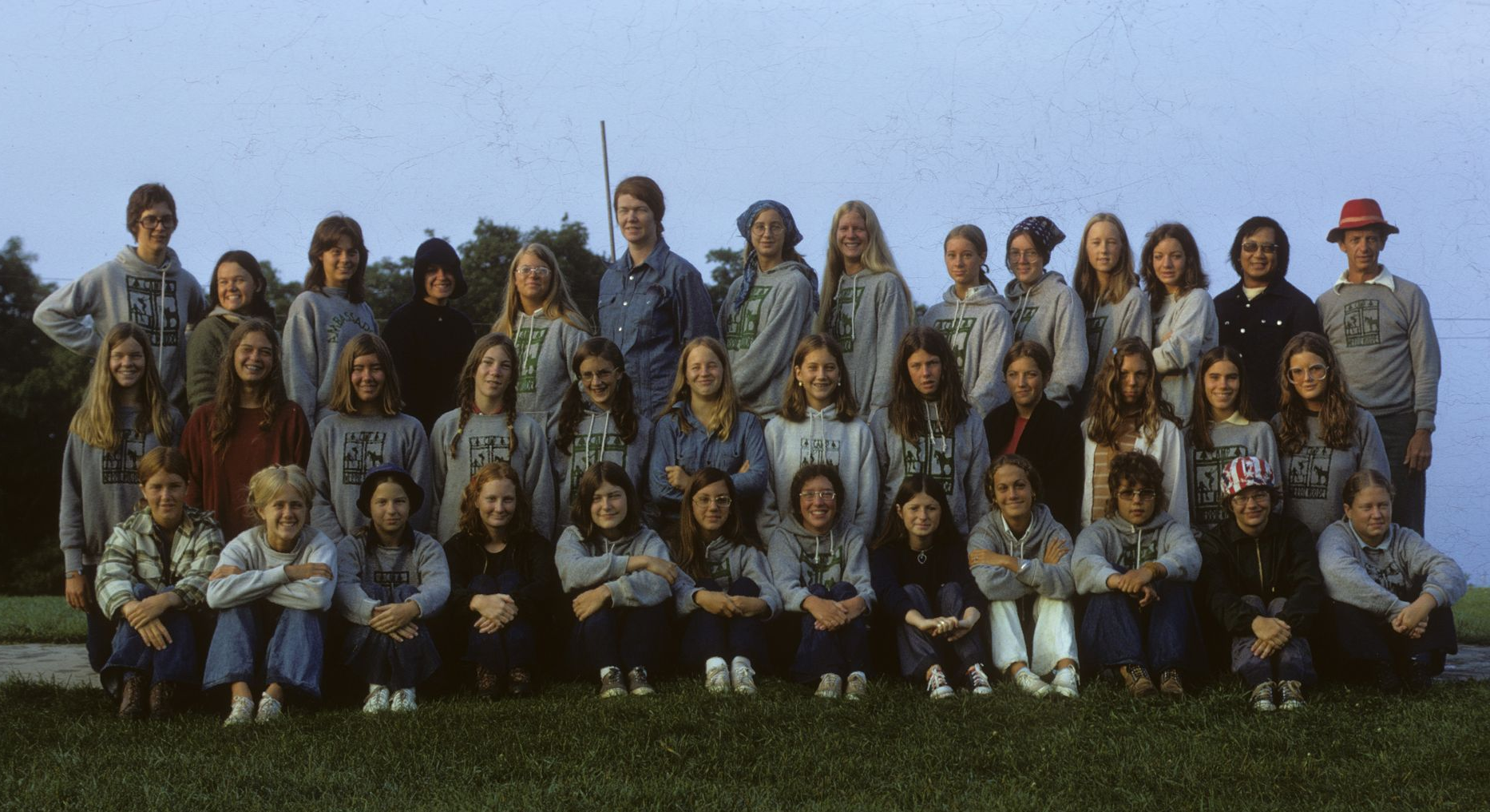 A group of people wearing matching sweatshirts pose for a portrait on a grassy field under an open sky.