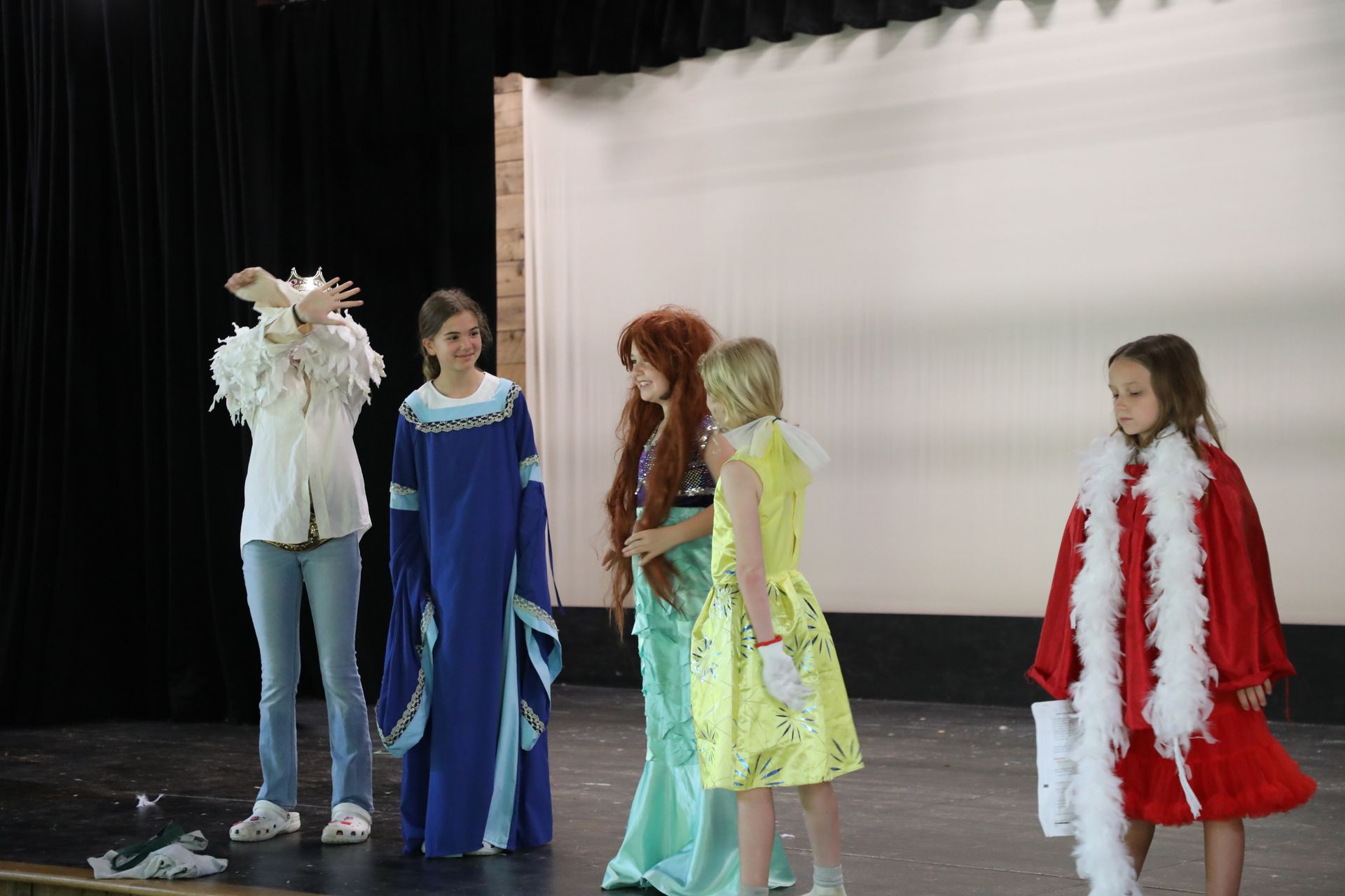 Five children in costume stand on a stage, some posing, during a performance or dress rehearsal.