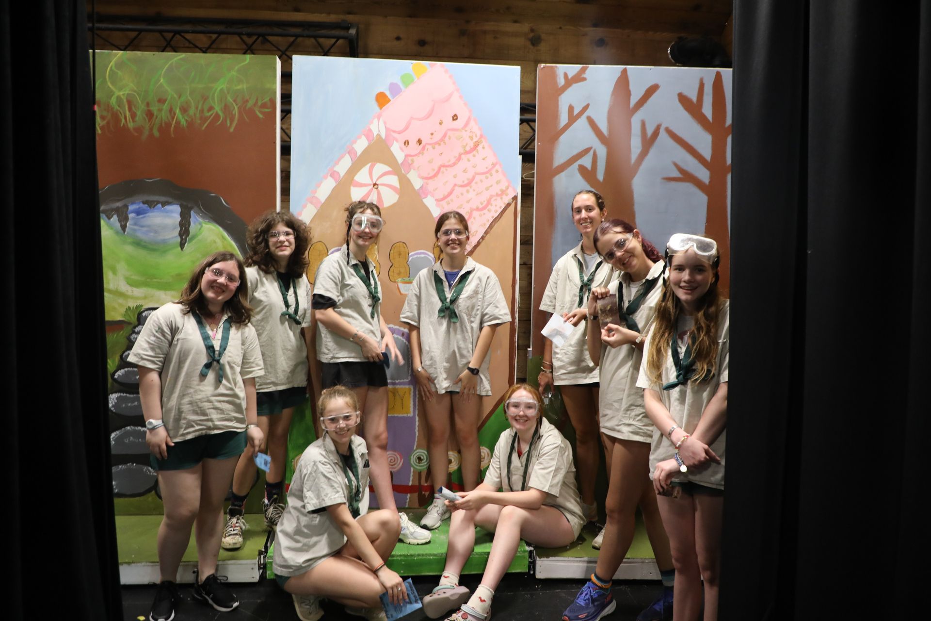 A group of people in matching shirts and scarves pose for a photo in front of hand-painted theatrical backdrops.