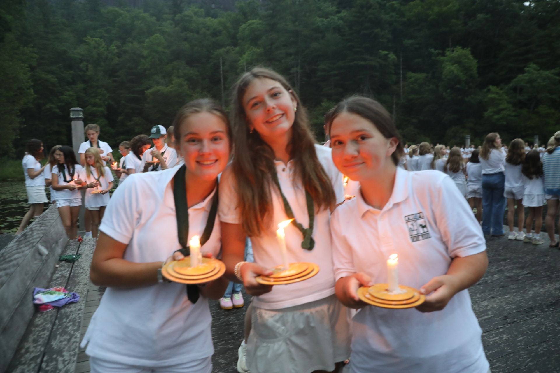 A person in a white shirt kneeling by a lake, placing a lit candle on a floating disk into the water.