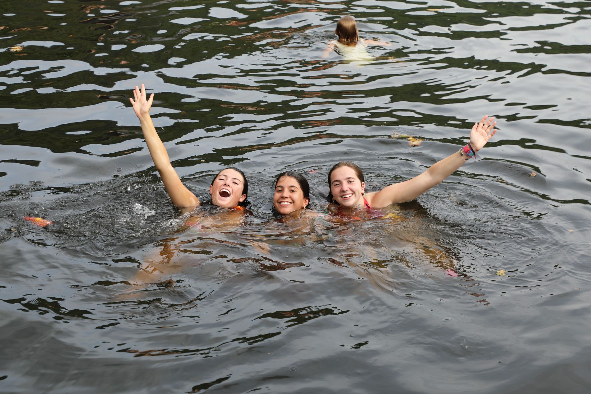 Three people smile while posing for a piggyback photo in front of a leafy green background.