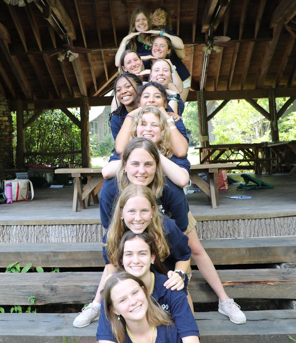 A group of people wearing blue shirts stacked in a pyramid formation, smiling in a wooden pavilion.
