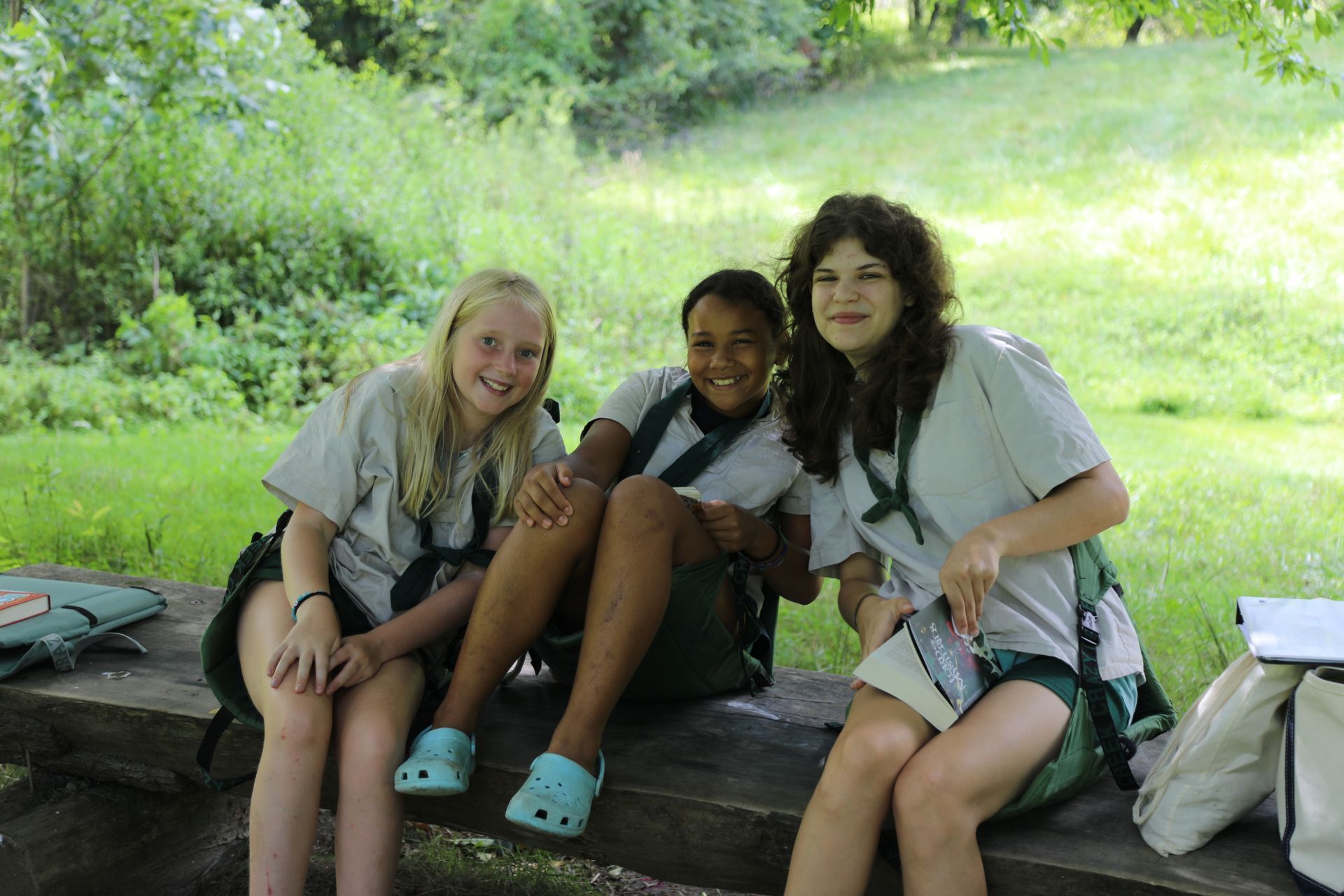 Two campers in tan uniform shirts and green shorts smiling with arms around each other next to wooden outdoor stairs.