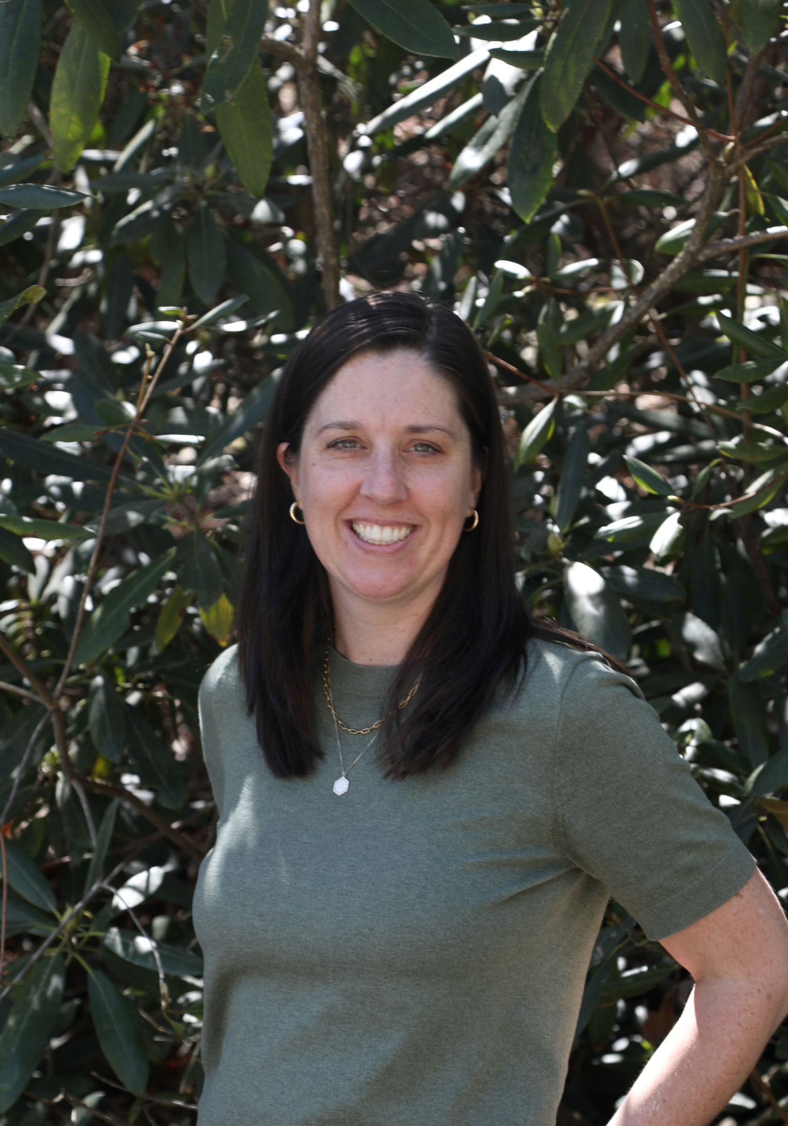 A professional headshot of a person with shoulder-length dark hair, smiling slightly against a plain white background.