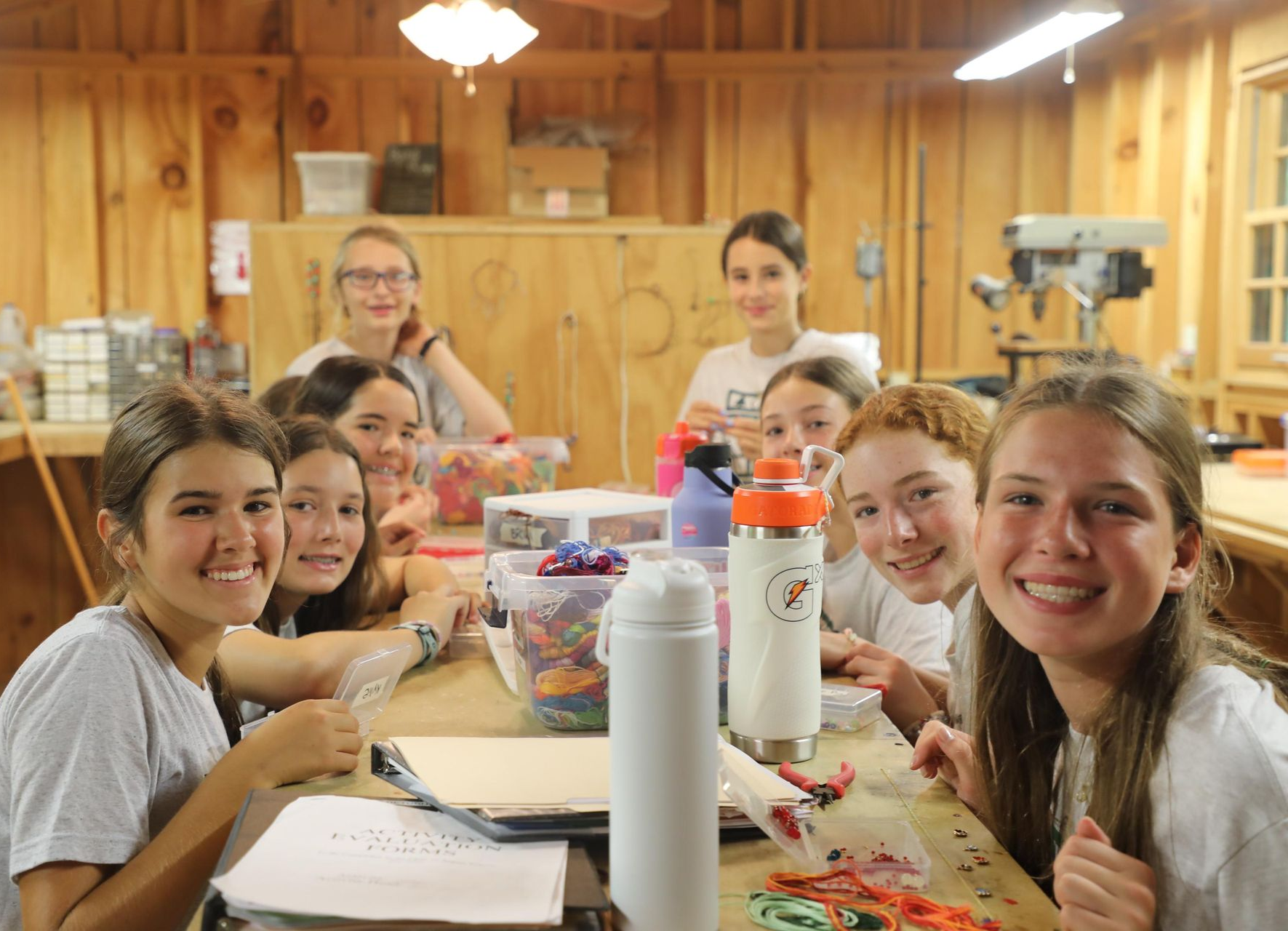 A group of people sitting around a wooden workbench in a workshop, smiling at the camera.