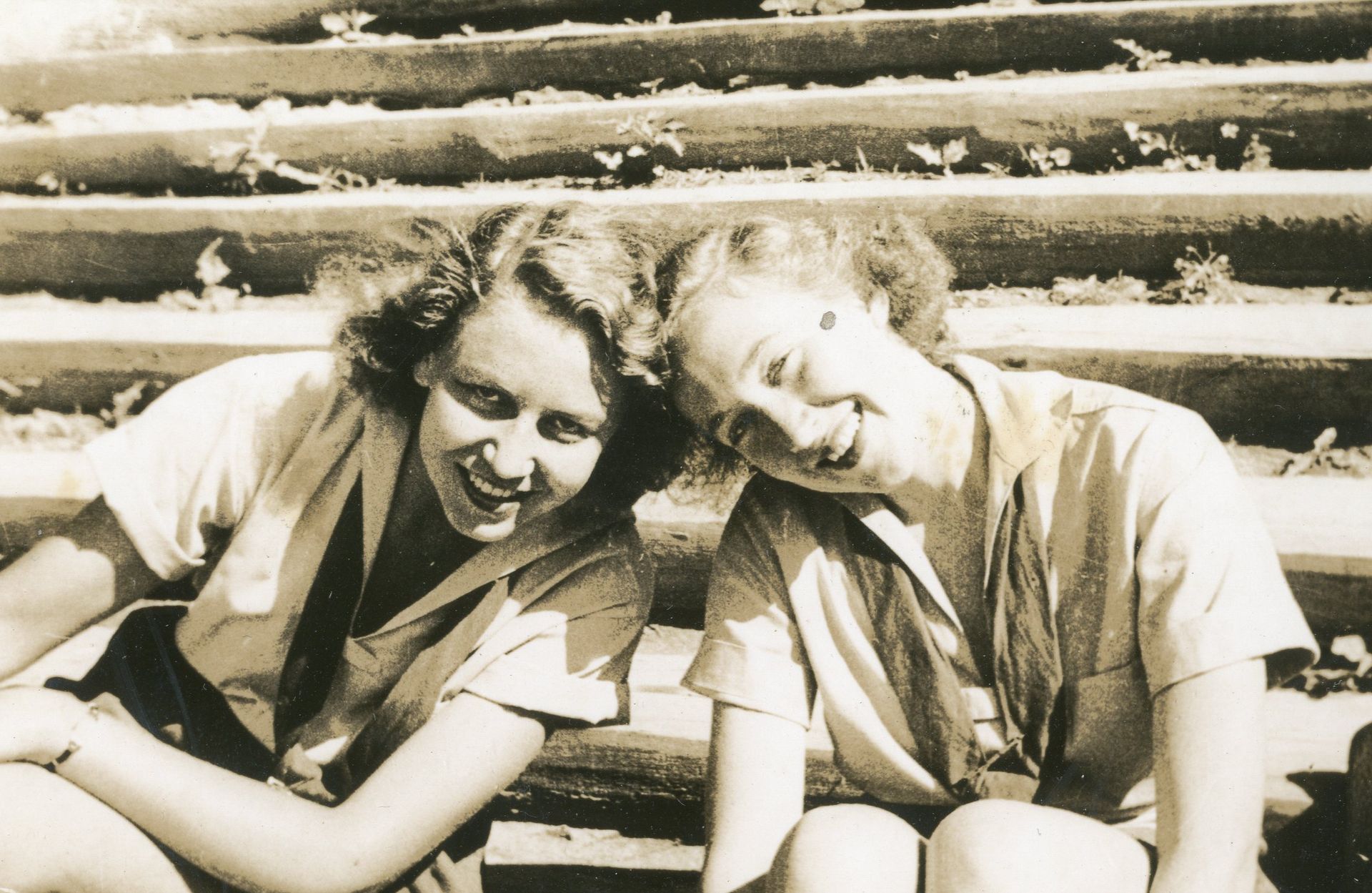 Two people sitting on concrete steps with their heads leaning together, both smiling and wearing collared shirts.