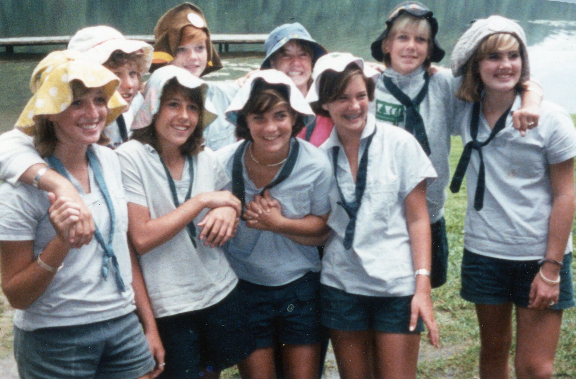 A group of eight people wearing matching shirts, shorts, and bucket hats posing together outdoors near a wooden dock.
