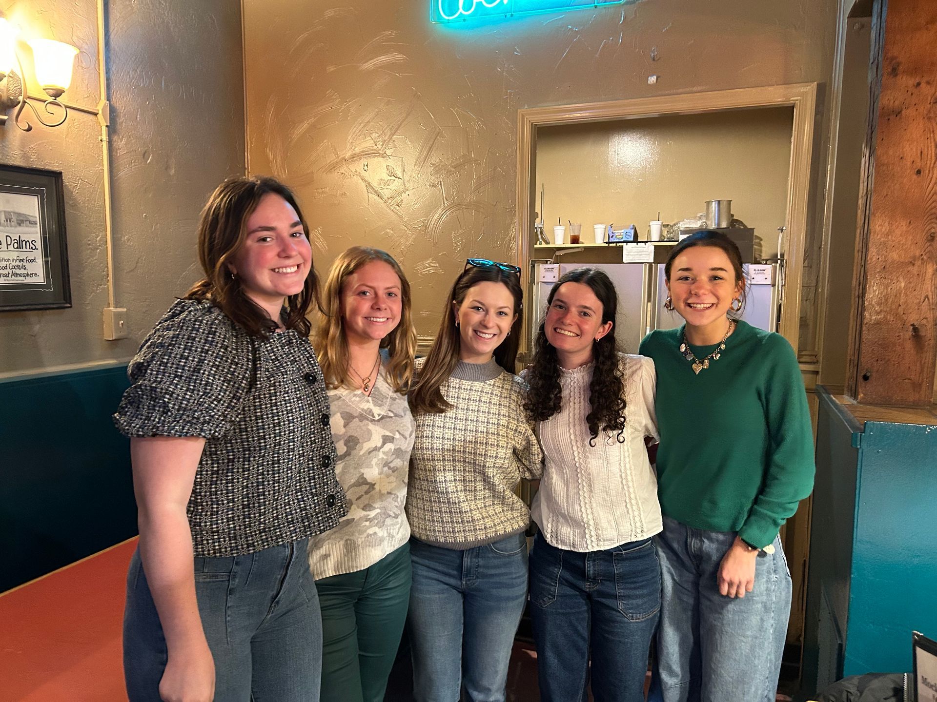 Five people stand together smiling for a photo in a casual, dimly lit restaurant setting.