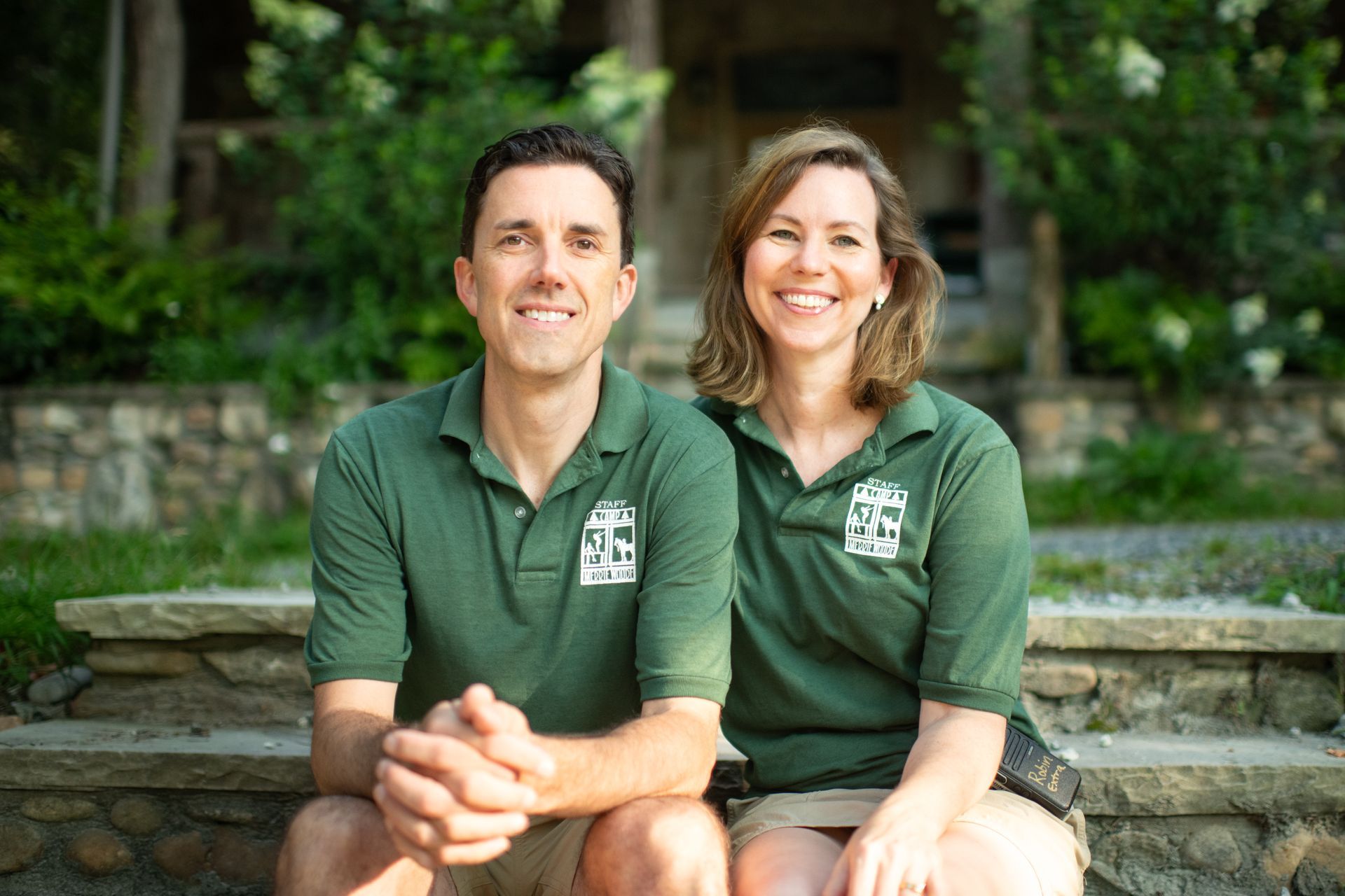 A smiling couple in matching green polo shirts sitting on stone steps outdoors.