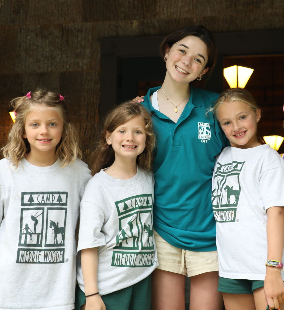 Four people smiling together, three wearing matching white shirts with green graphics and one in a dark green polo shirt.