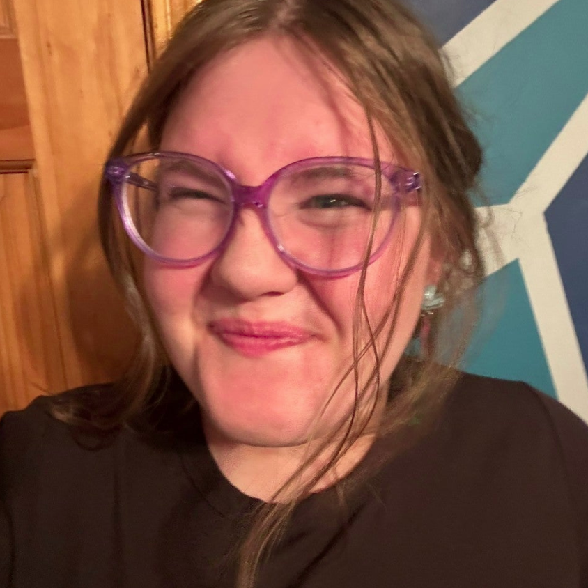A smiling person wearing glasses and a 