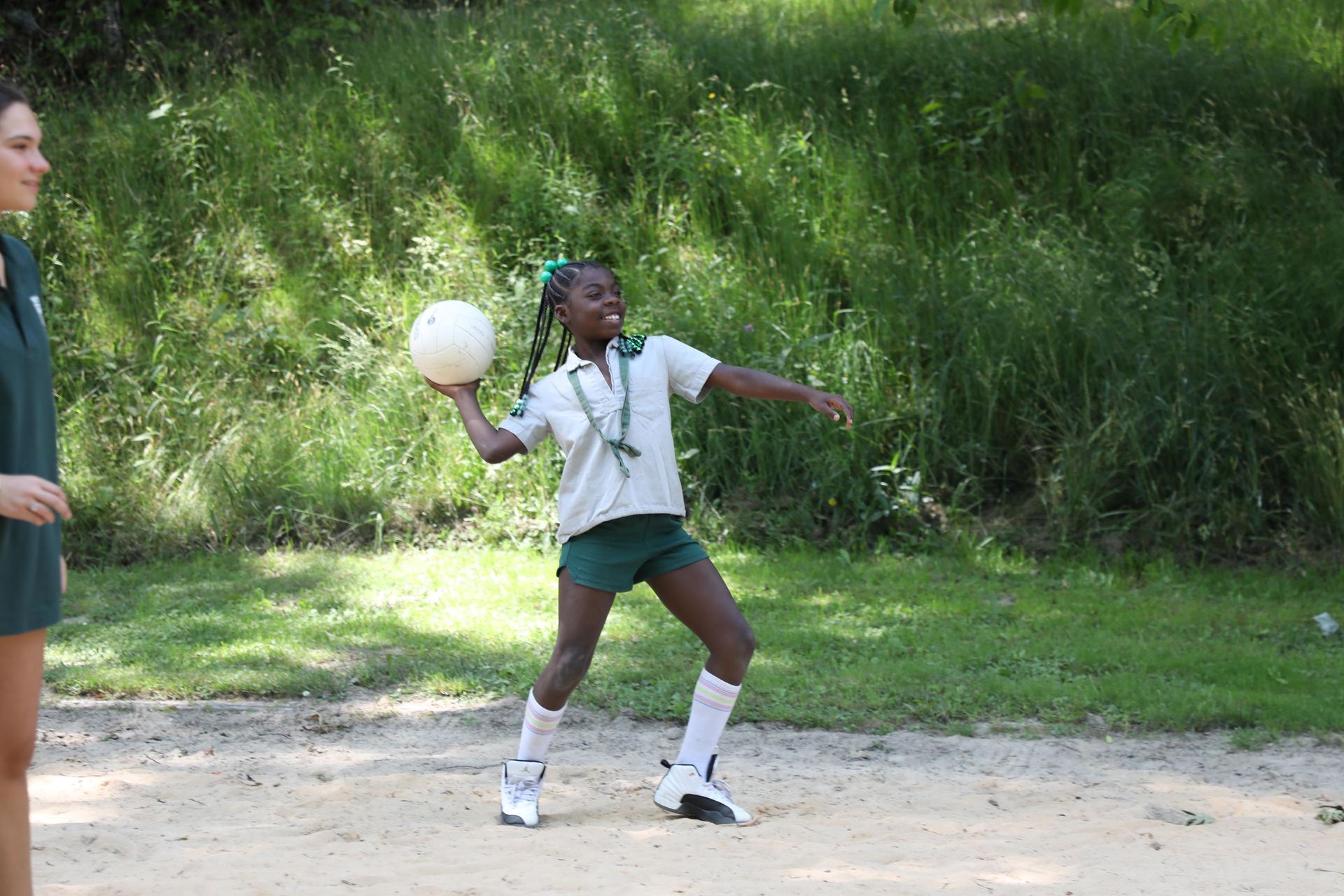 A person in a white polo and dark shorts throwing a white ball in a park setting.