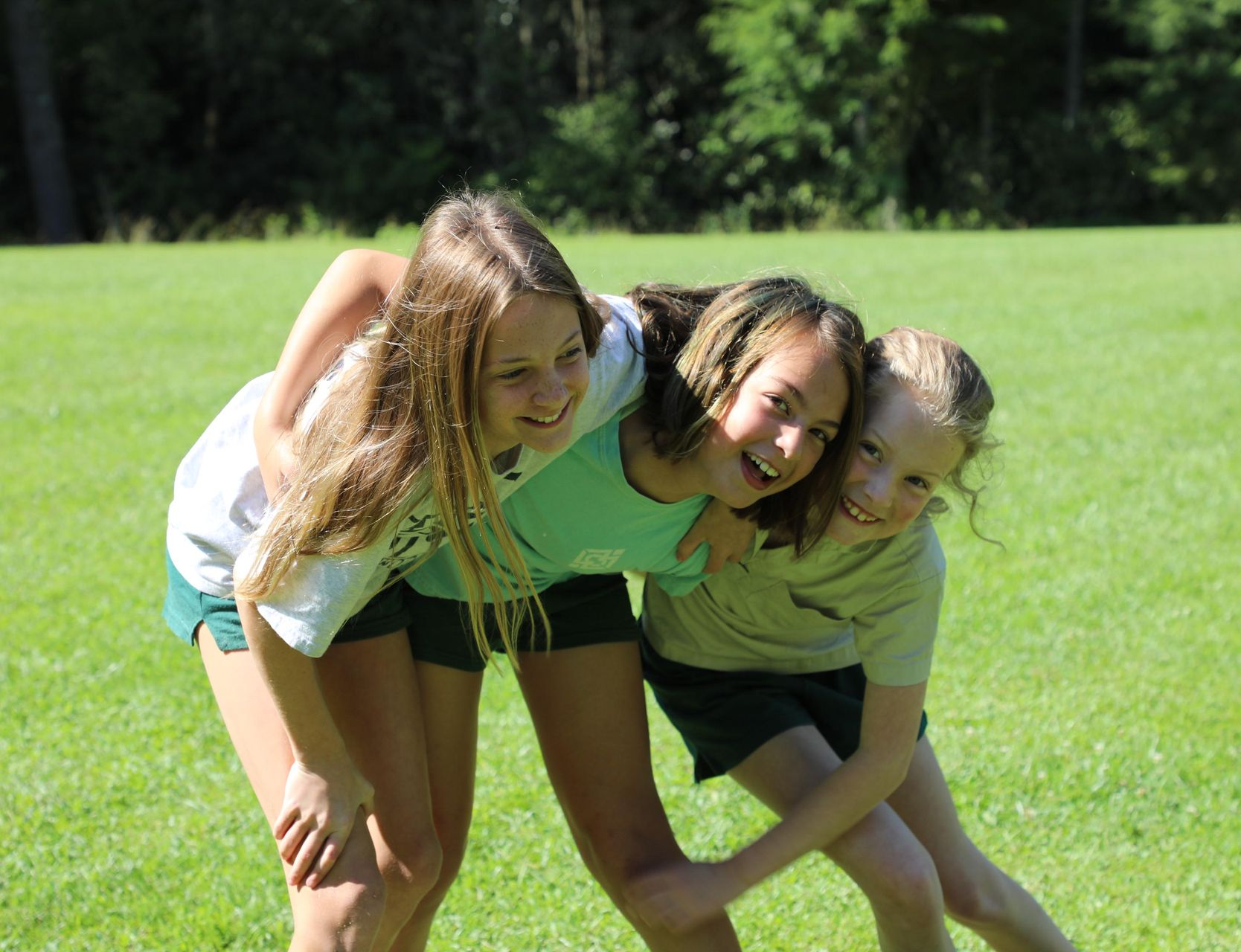 Three individuals in athletic wear embrace while laughing in a grassy field.
