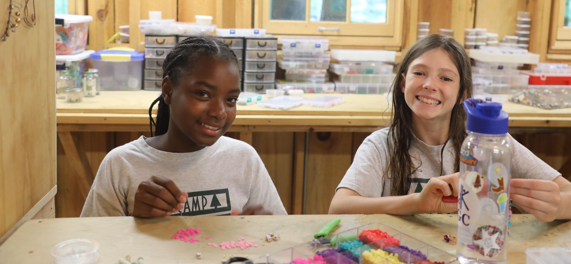 Two smiling individuals work on a craft project at a wooden table in a well-stocked art studio.