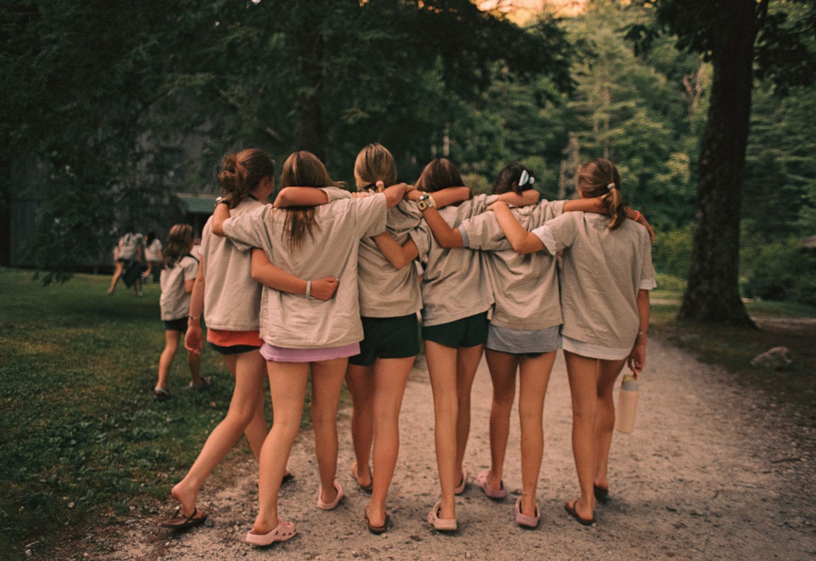 A group of smiling people form a human pyramid on a grassy field in front of a sand volleyball court.