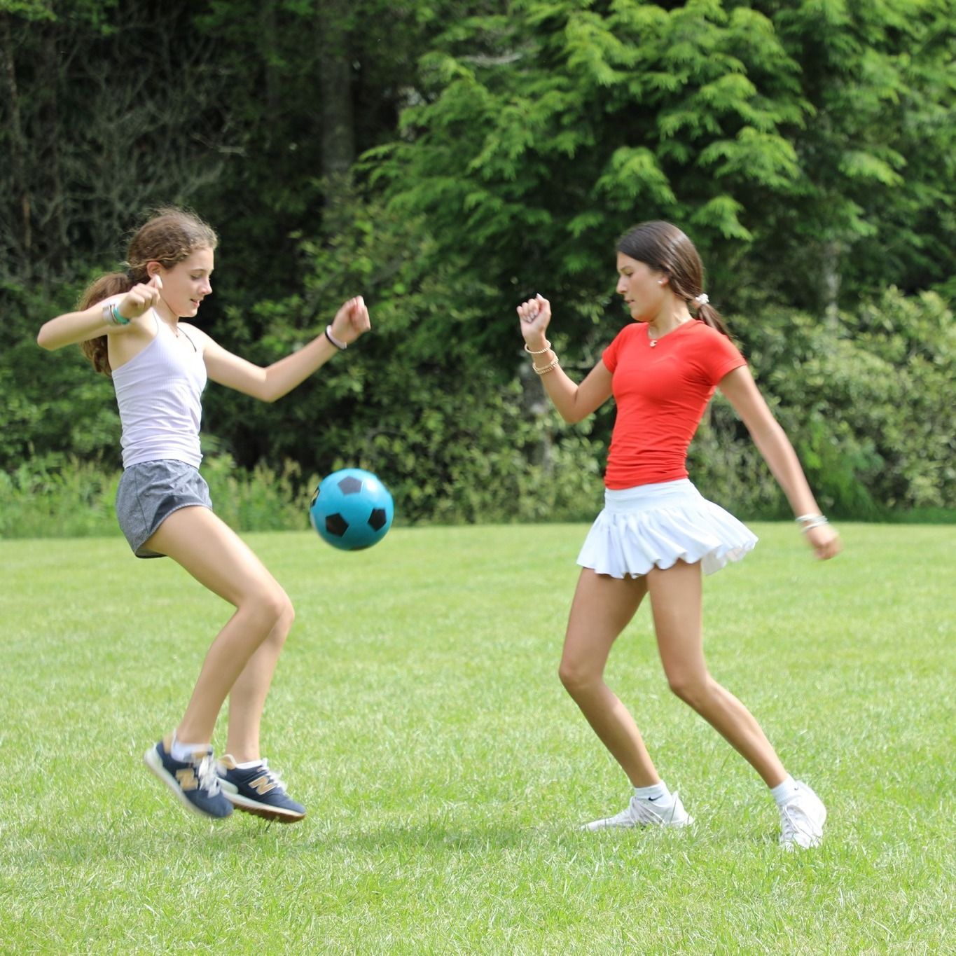 Two people in an outdoor field playing with a blue soccer ball, one leaping to kick it while the other watches.