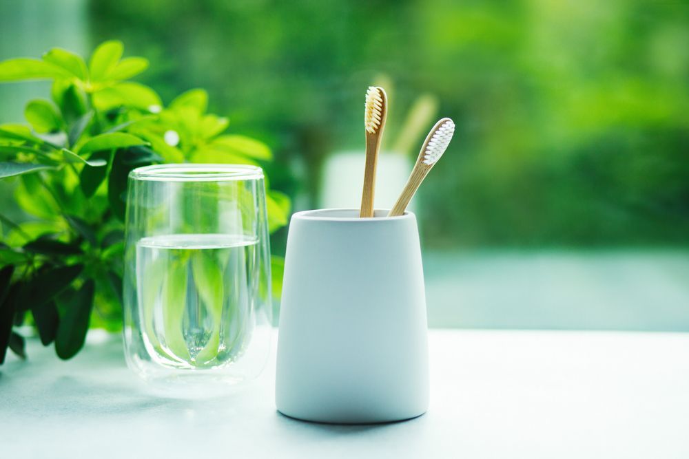 Toothbrushes in a Cup Next to a Glass of Water — Dr John Salmon, Kiama Family Dental In Kiama, NSW