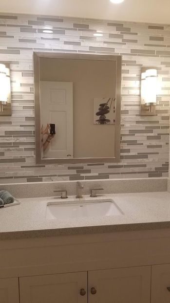 Bathroom vanity with white sink, large mirror, and mosaic tile backsplash above cabinet drawers