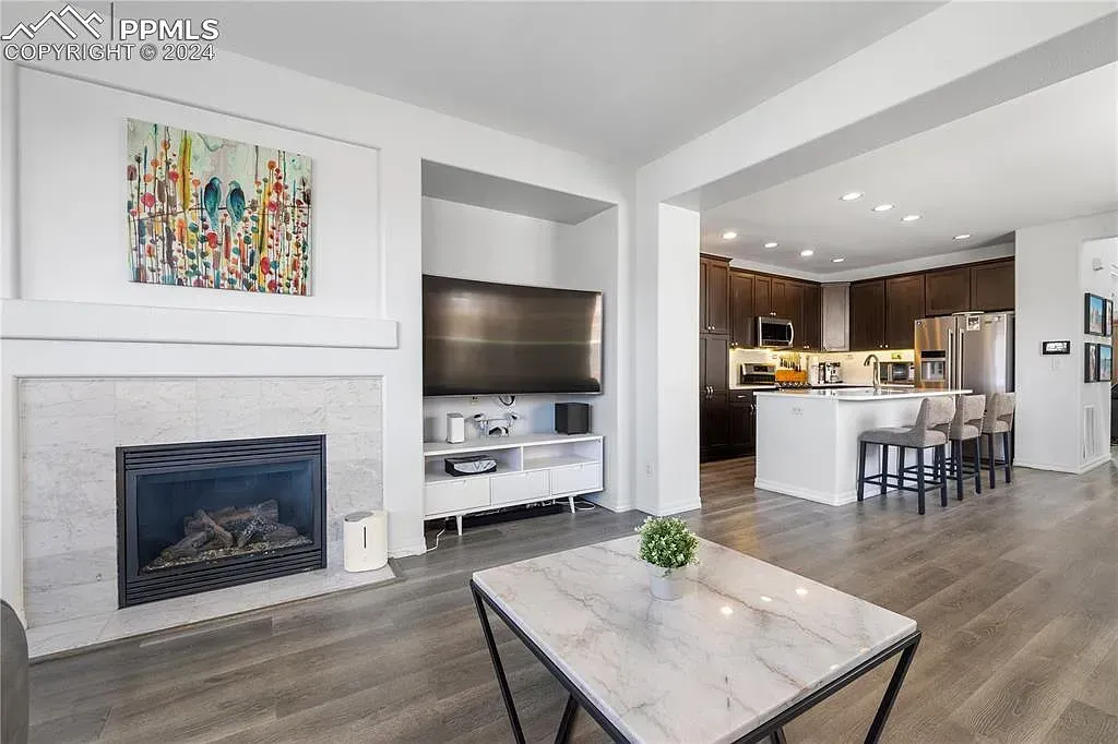 Bright open-plan living room with fireplace, TV, coffee table, and adjoining kitchen with island and barstools
