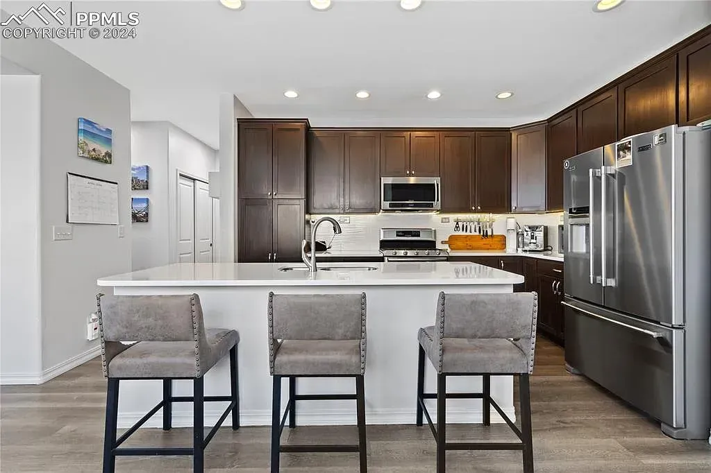 Modern kitchen with white island, three gray stools, dark cabinets, and stainless steel appliances