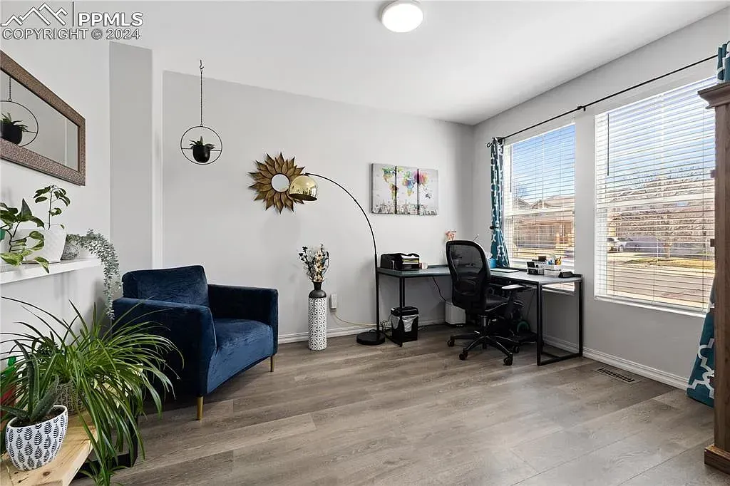 Bright home office with blue chair, desk, large window, plants, and wall decor