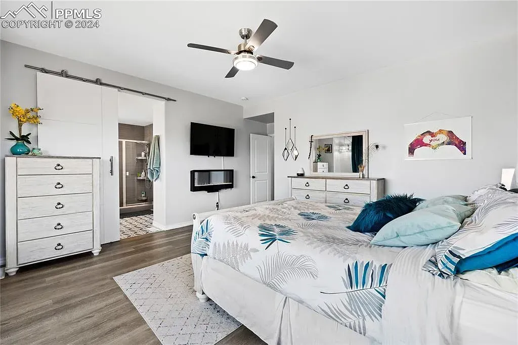 Bright white bedroom with a bed, dresser, wall-mounted TV, and ceiling fan.