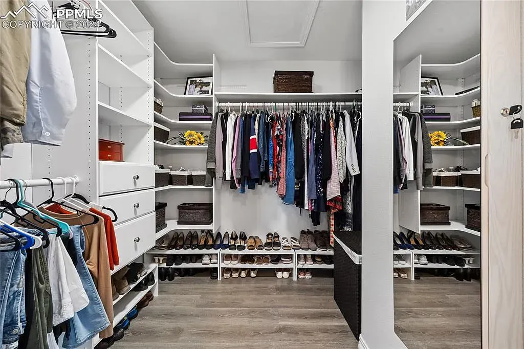 Spacious walk-in closet with hanging clothes, shelves, shoes, and a bench in a bright room