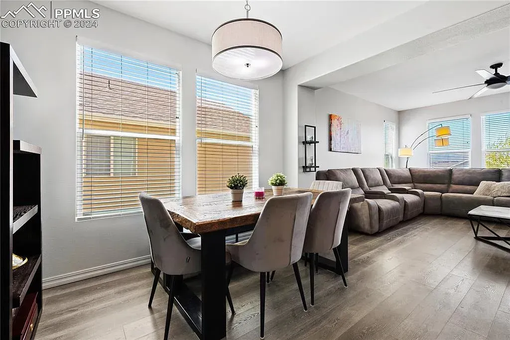 Bright dining area with dark table, gray chairs, and adjacent living room with sectional sofa and ceiling fan
