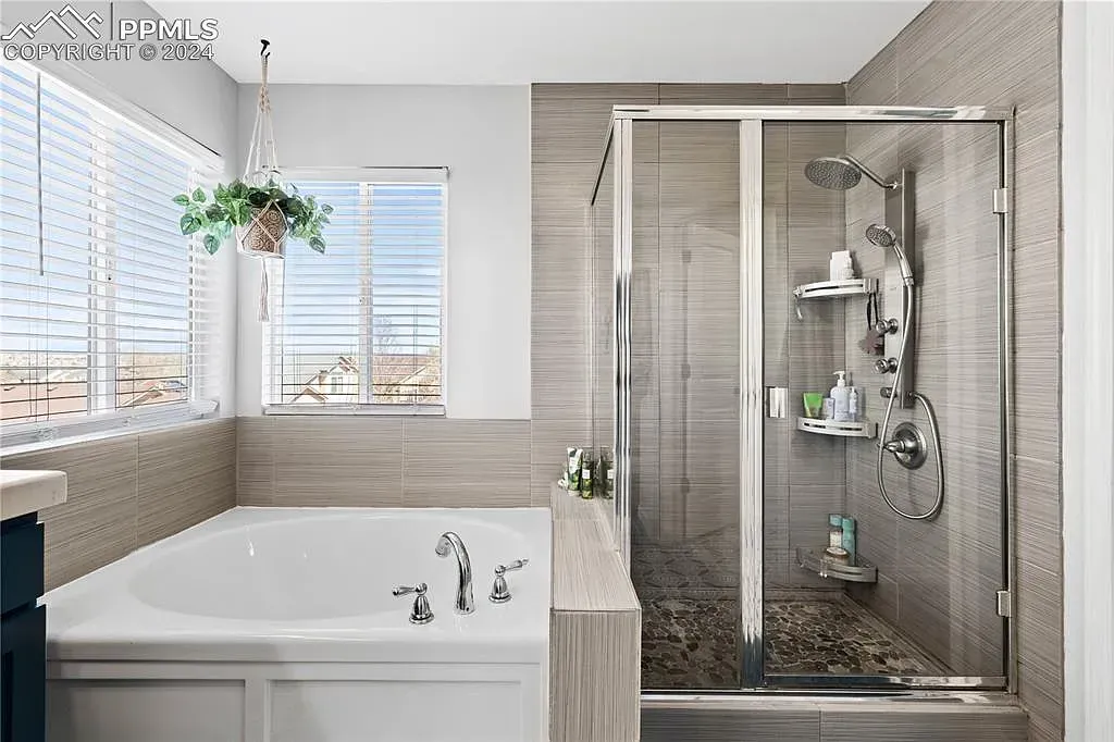 Modern bathroom with a bathtub, glass shower, and large windows with plants