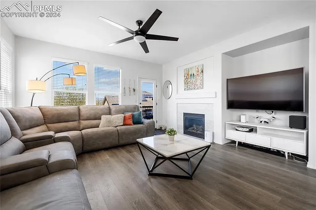 Modern living room with gray sectional, wall-mounted TV, fireplace, and coffee table on dark wood floors