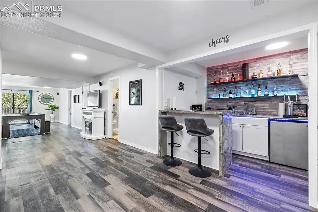 Bright modern lounge with gray floors, white walls, and a small bar area with stools and blue lighting