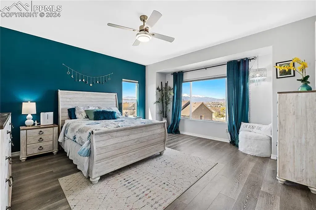 Bright bedroom with teal accent wall, white bedding, large window, and blue curtains