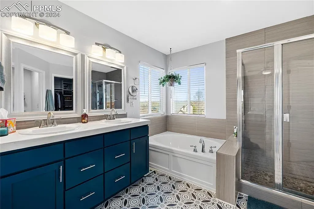 Bright bathroom with navy vanity, double mirrors, freestanding tub, and glass shower