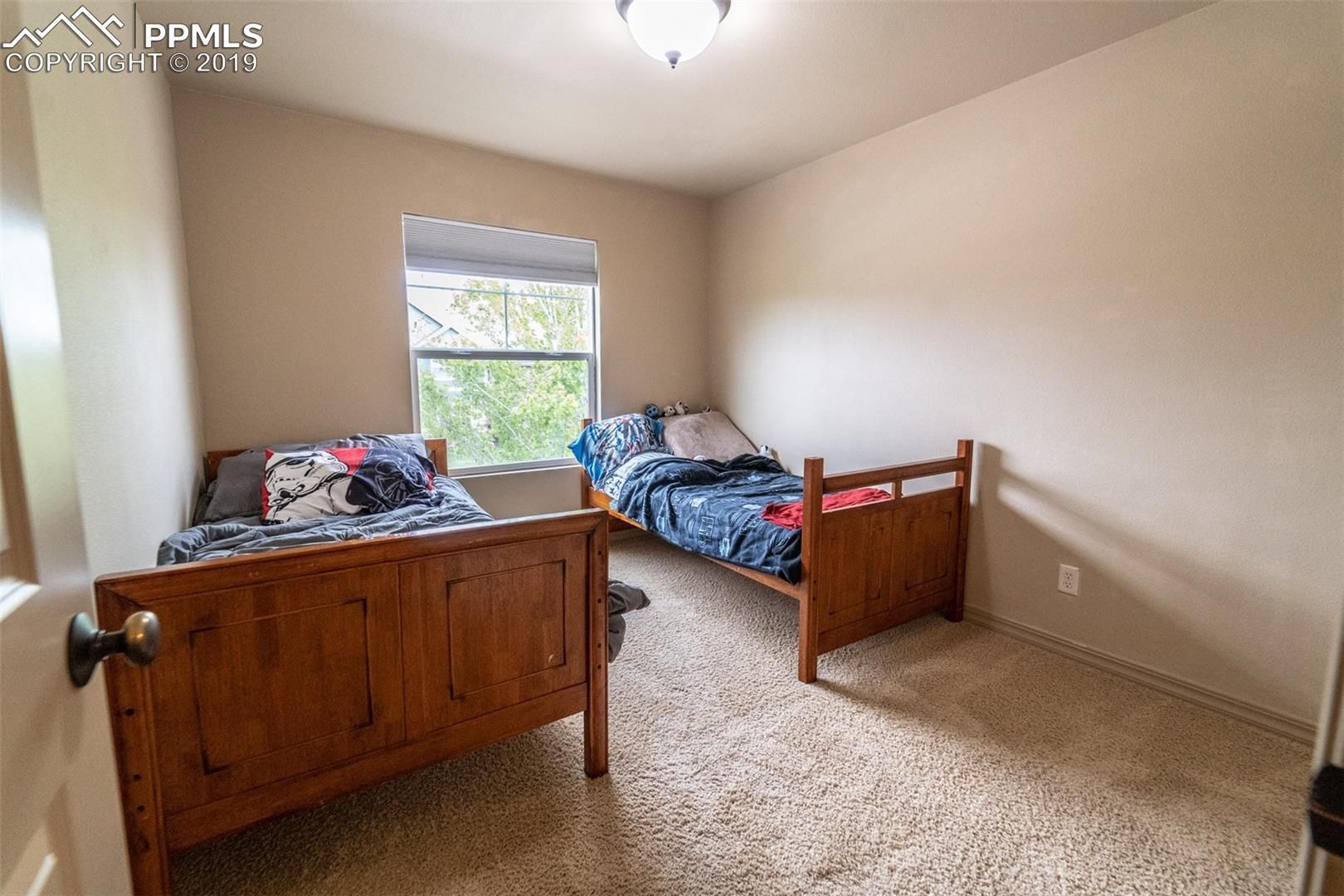 Small beige bedroom with two wooden twin beds, a window, and carpeted floor