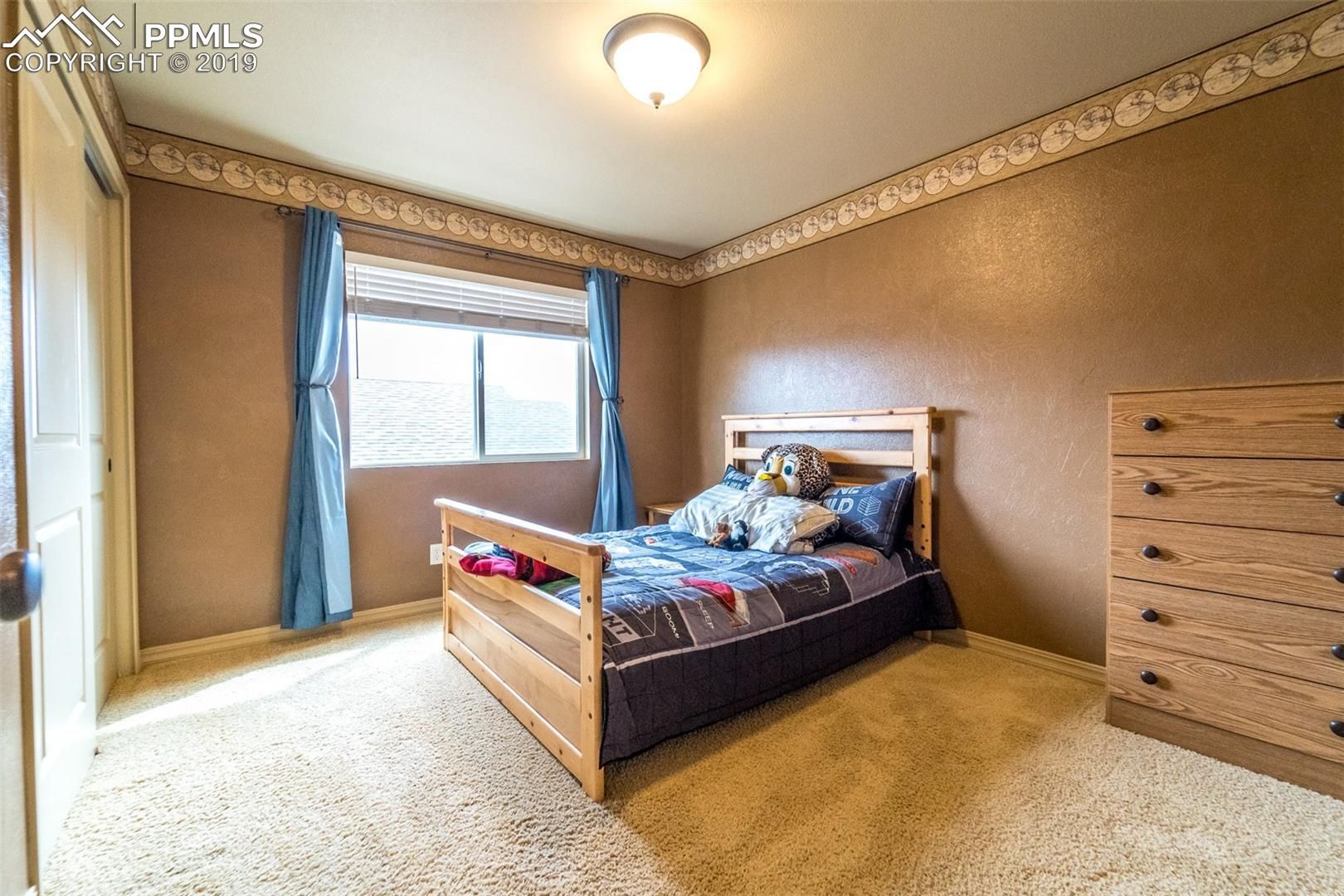 Bright bedroom with a wooden bed, dresser, blue curtains, and a window with a valance.
