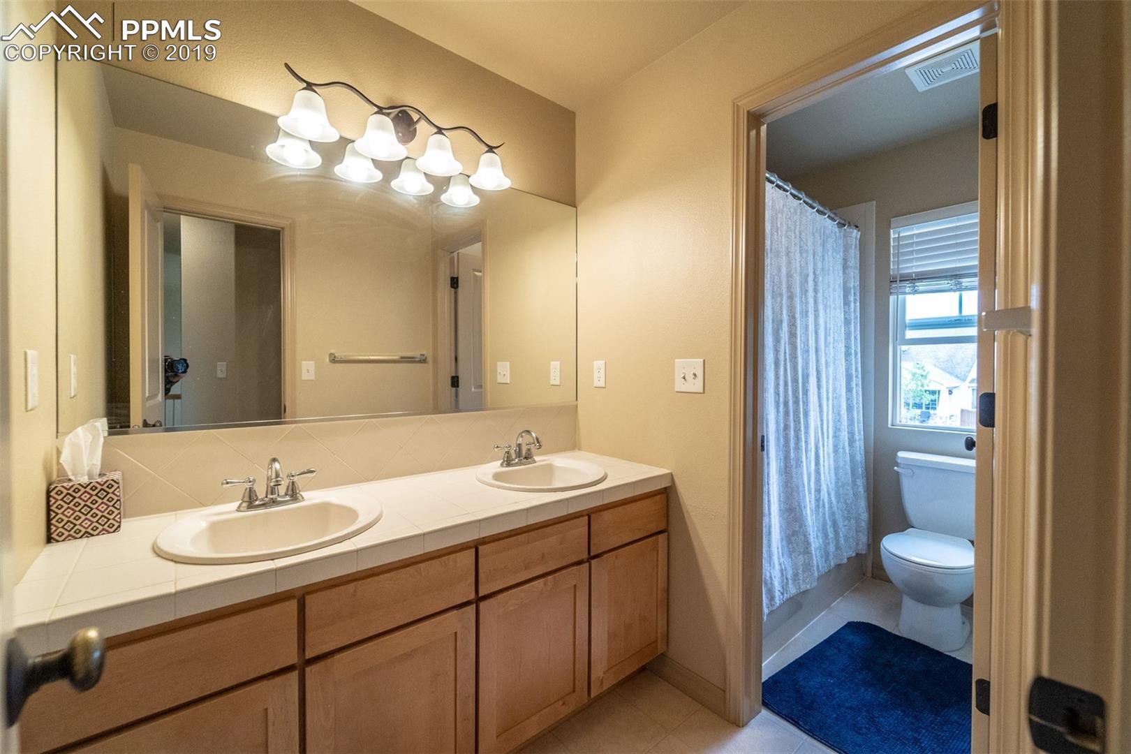 Bathroom vanity with double sinks, large mirror, and doorway to a toilet and shower area