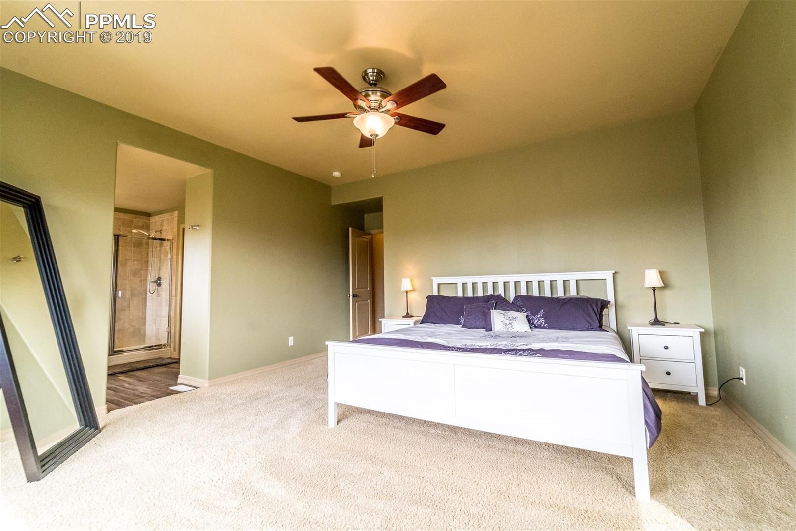 Spacious bedroom with white bed, nightstands, ceiling fan, and beige carpet in soft green walls