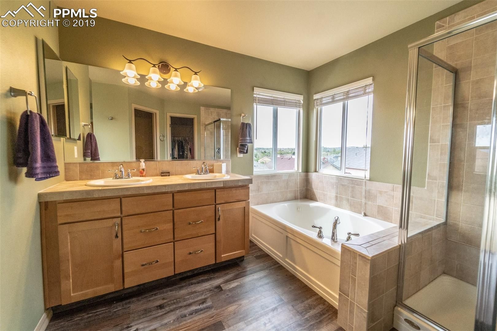 Spacious bathroom with wood vanity, double sinks, large soaking tub, walk-in shower, and beige tile accents