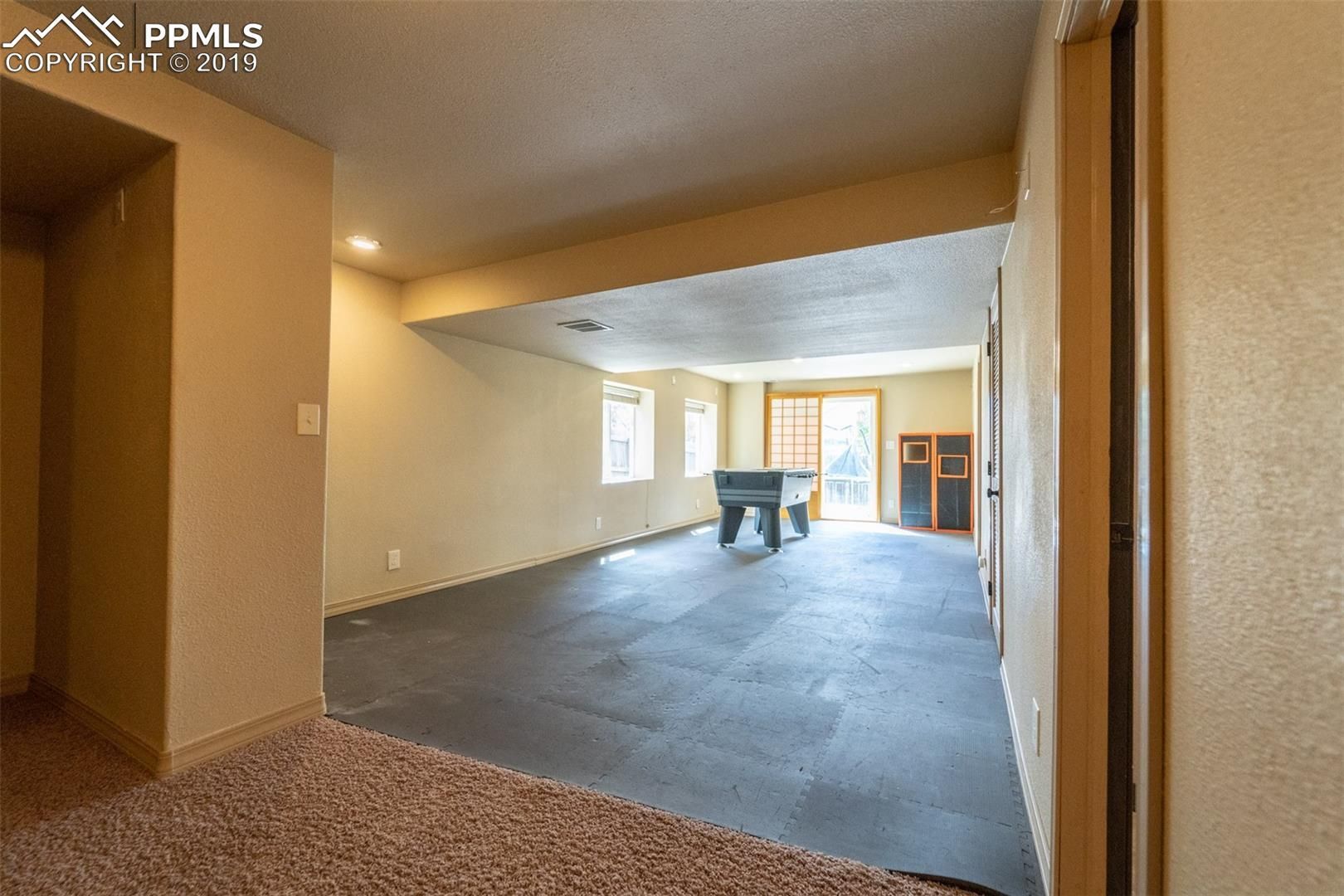Empty living room with carpet, beige walls, and a bright dining area in the back
