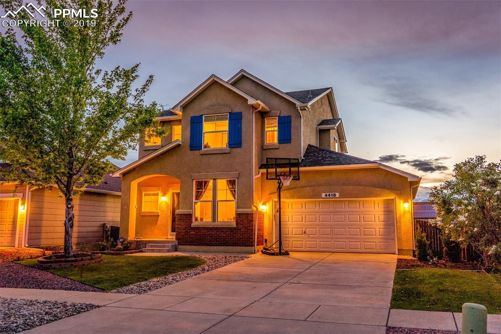 Two-story suburban house at dusk with warm porch lights and a two-car garage