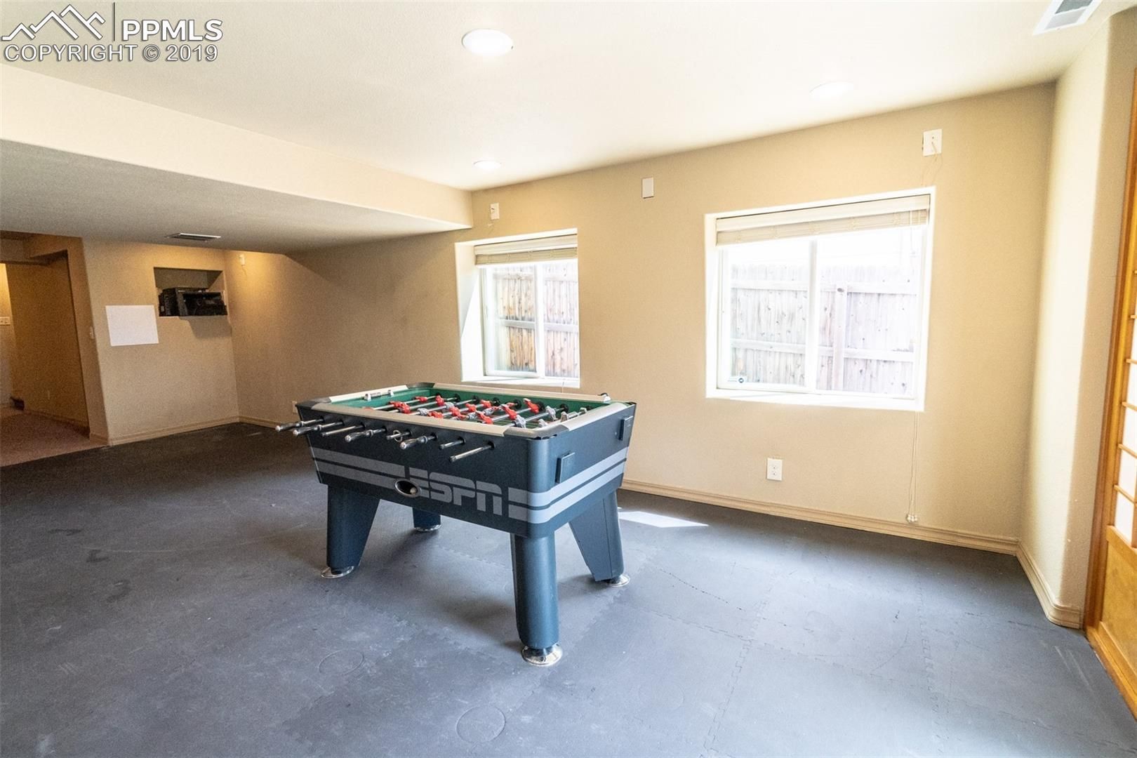 Spacious game room with a pool table, beige walls, and two windows letting in daylight