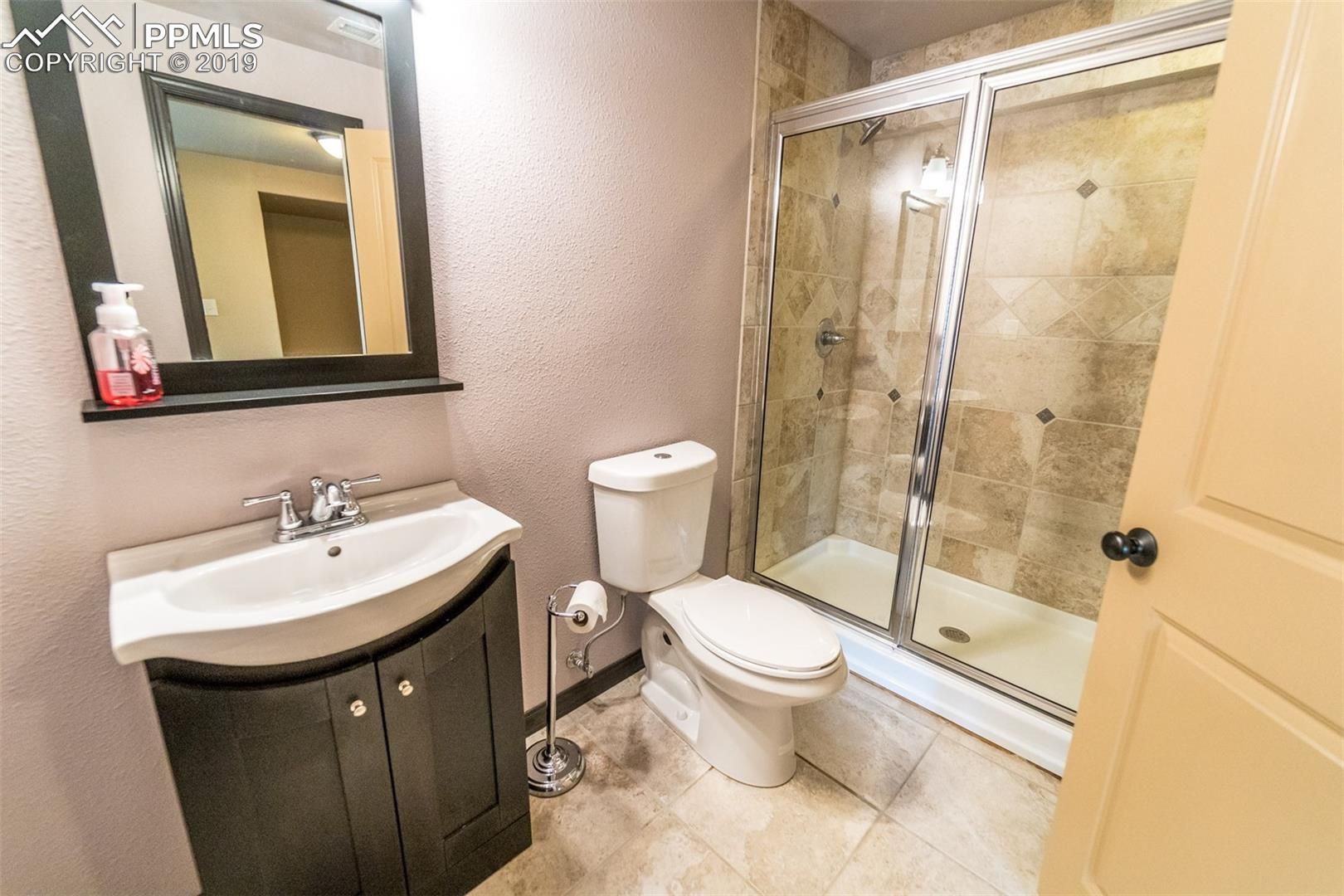Small beige bathroom with vanity, toilet, and glass shower enclosure