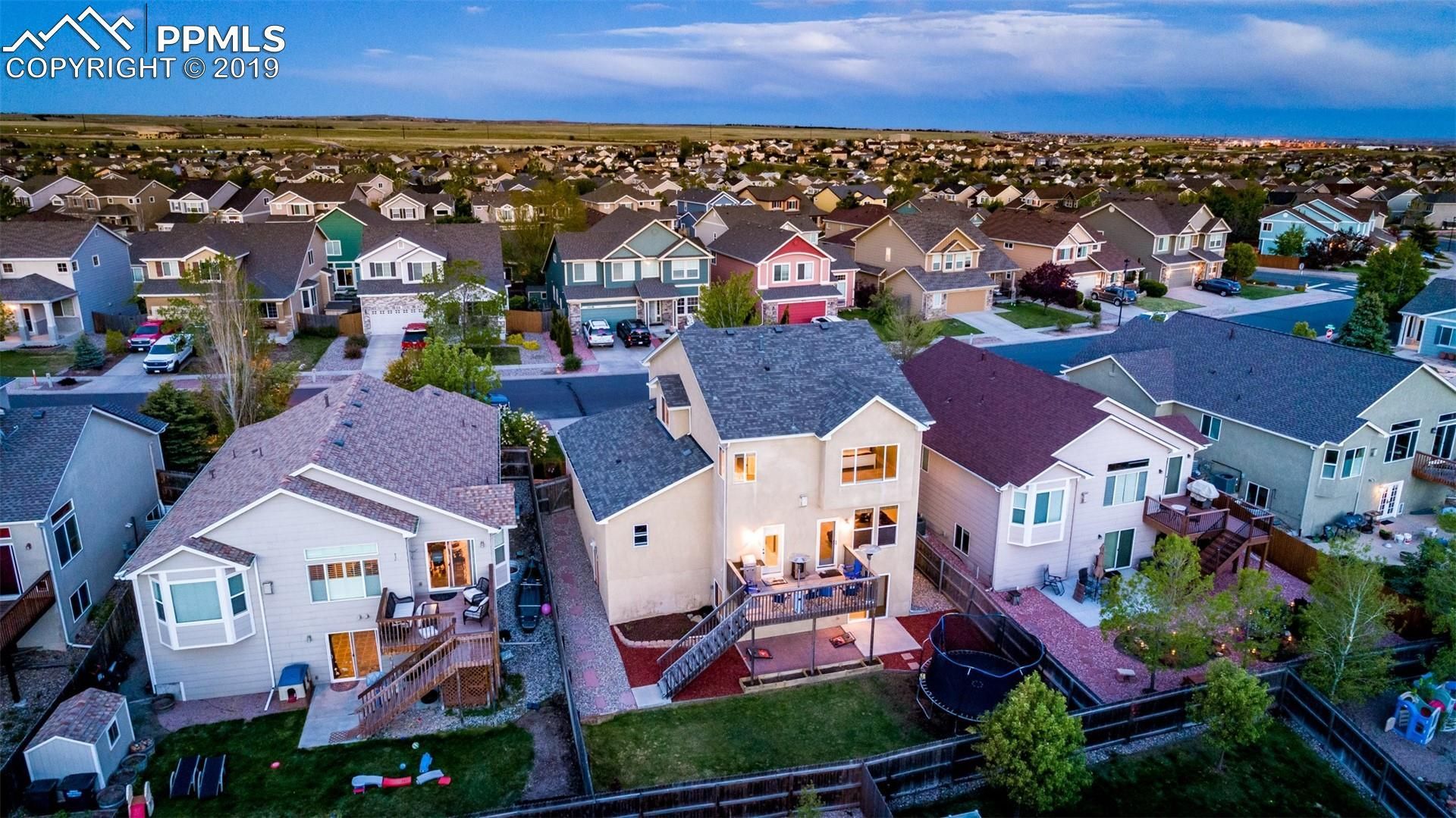 Aerial view of a suburban neighborhood with rows of houses at dusk, including a lit two-story home in the foreground.
