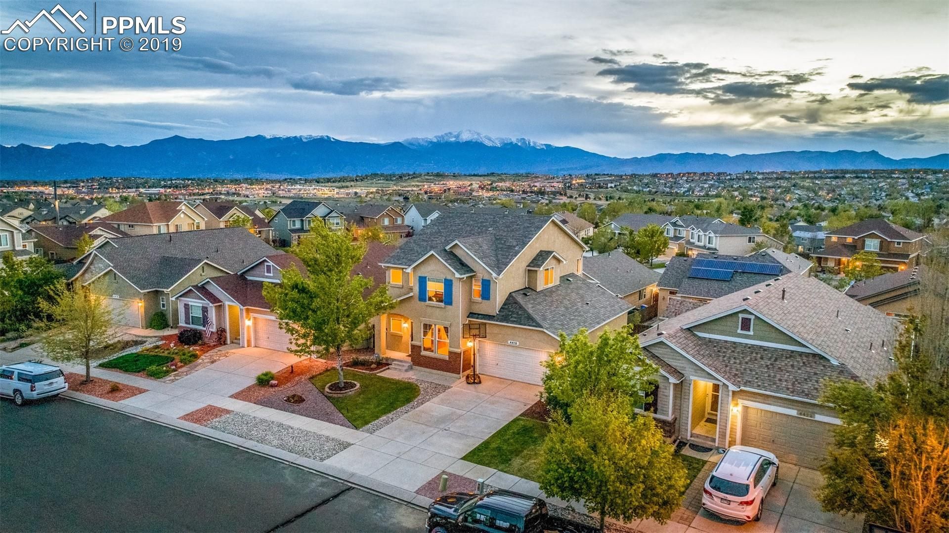 Aerial view of a suburban neighborhood with lit homes and mountains under a cloudy dusk sky