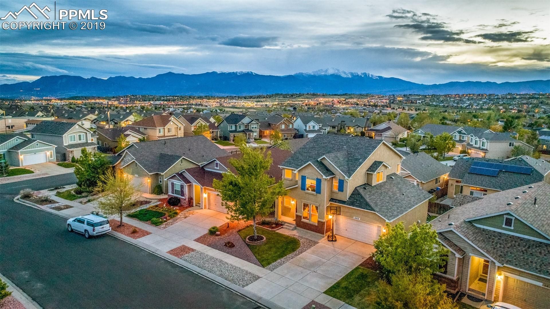 Suburban neighborhood at dusk with lit homes, palm trees, and mountains in the background
