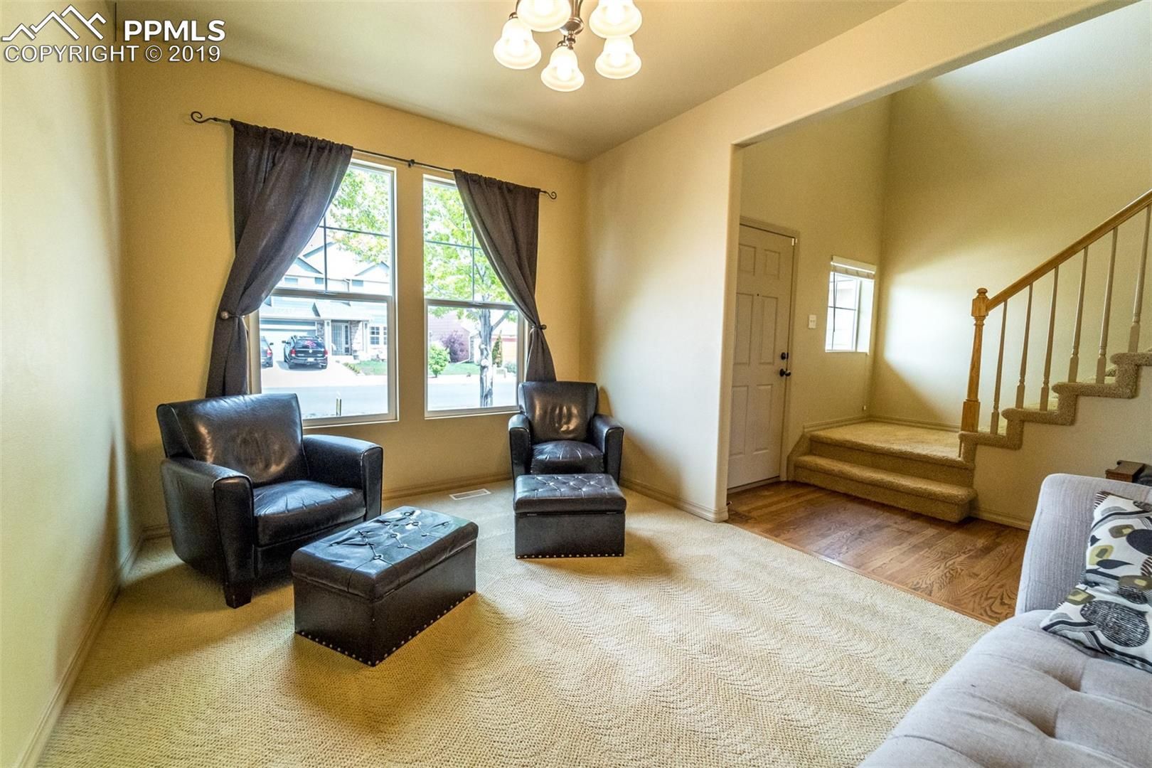 Bright beige living room with two black chairs, ottoman, window, stairs, and tufted sofa edge.