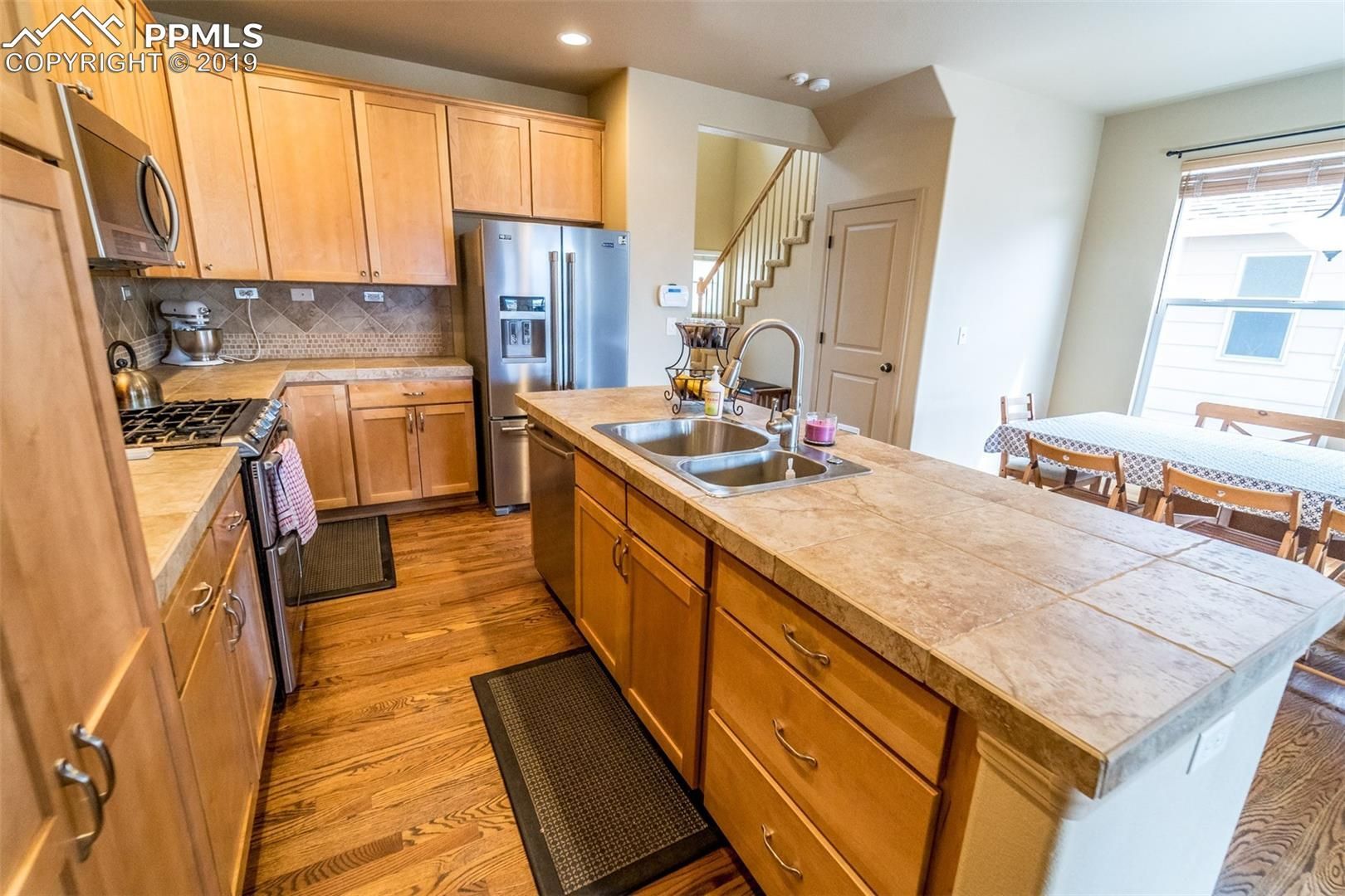Kitchen with wood cabinets, island countertop, sink, and stairs in the background.